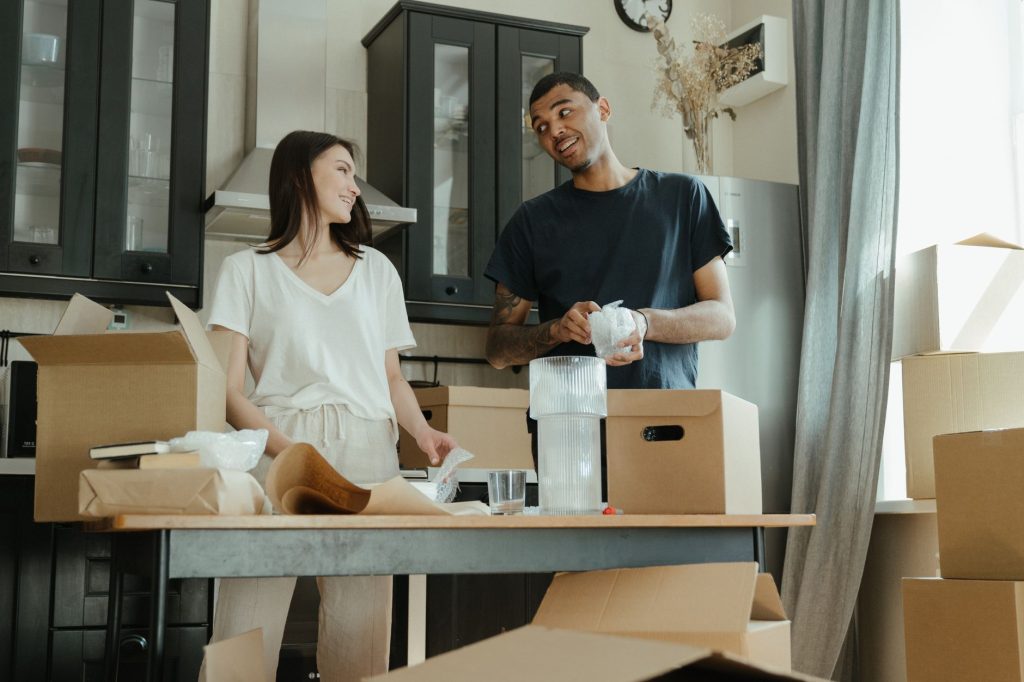Smiling couple unpacking boxes in their new home kitchen, ready for a fresh start. — Booking a Rat Pack Tribute Show - Mistak