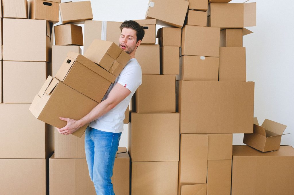 Young unshaven guy in casual clothes carrying stack of heavy cardboard boxes during relocation into new apartment — "Stockhol