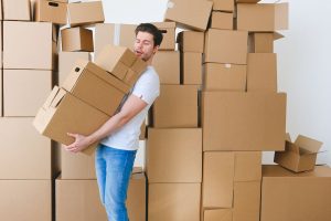Young unshaven guy in casual clothes carrying stack of heavy cardboard boxes during relocation into new apartment — "Stockhol